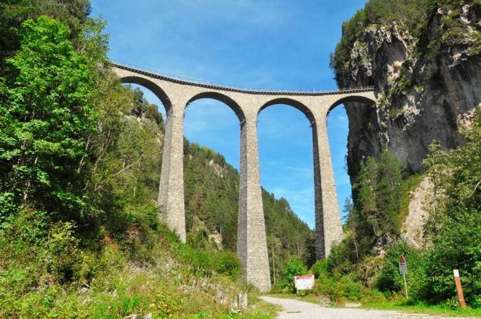 Pasarás por el Viaducto de Landwasser de 213 pies de alto (65 m), rodeado de altos árboles y montañas.